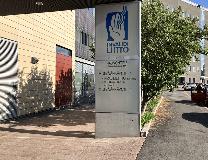 Nauvontien puoleisen sisäänkäynnin opaste, jossa on Invalidiliiton logo ja opastus sisäänkäynneille