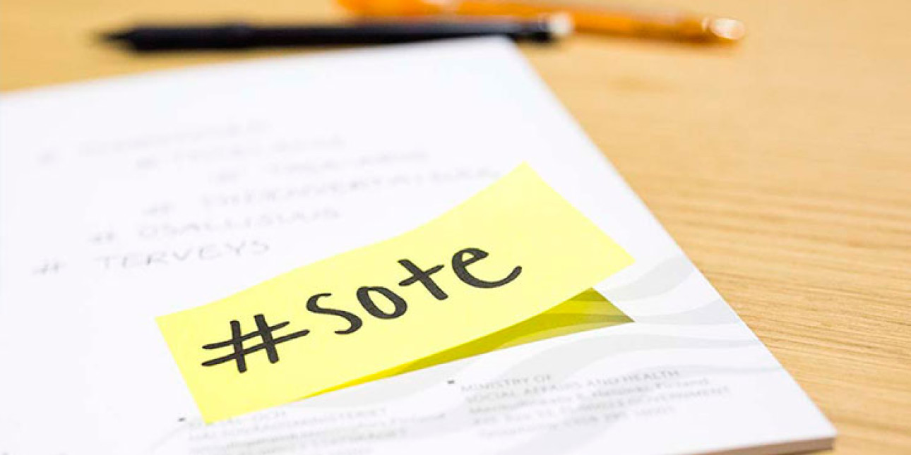Pöydällä kynä, paperi ja muistilappu, jossa lukee sote