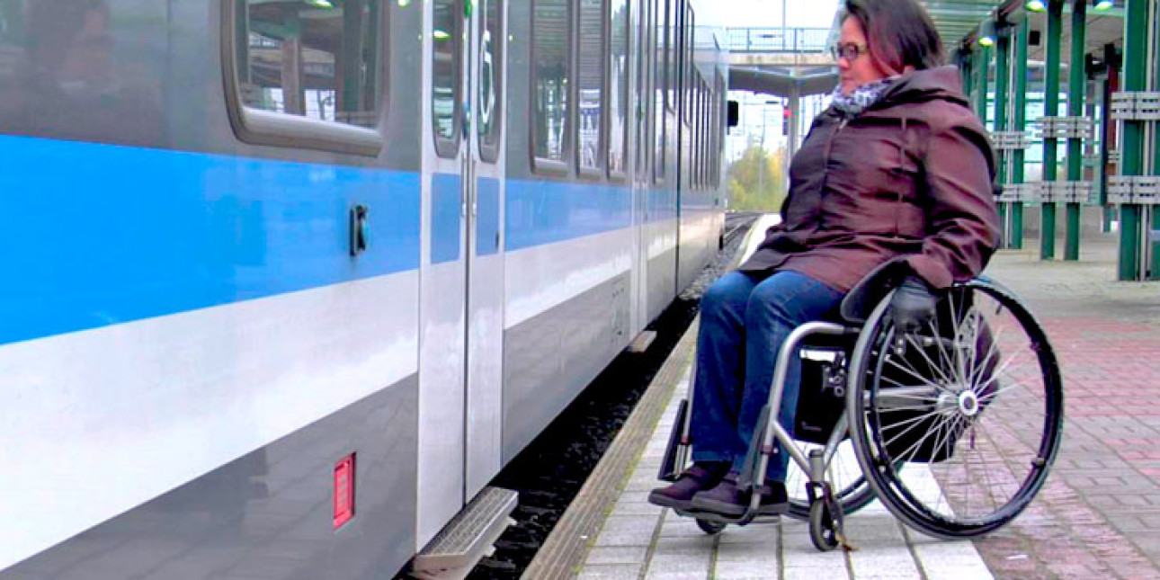 Pyörätuolilla liikkuva henkilö asemalaiturilla menossa junaan