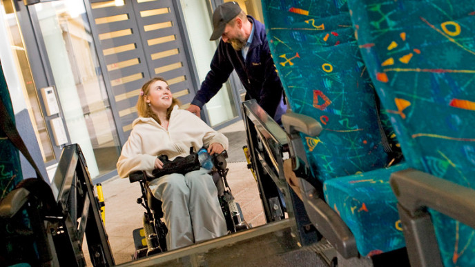 Nuorta pyörätuolissa istuvaa naista avustetaan inva-taksiin. Kuvituskuva.