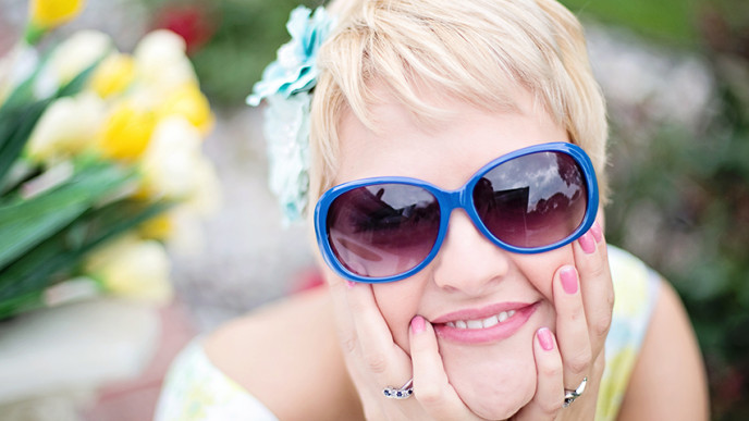 Kesäinen kuva, jossa nainen hymyilee kameralle aurinkolasit päässä.