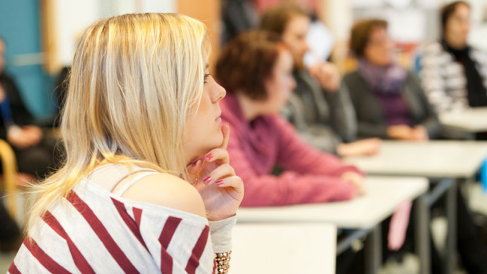 Vaaleahiuksinen tyttö seuraa opetusta pulpetissa. 