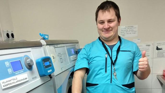 Nico Tikkakoski työpaikallaan pesulassa sinisessä työasussa peukalo ylhäällä.