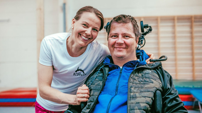 Volttimedia Oy:n toimitusjohtaja Sanna Mönkkönen miehensä kanssa liikuntasalissa. Taustalla puolapuut.