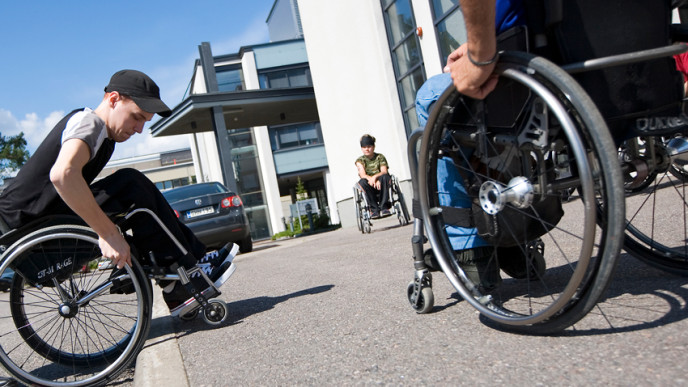 Kolme ihmistä kelaa pyörätuoleissa pihalla.