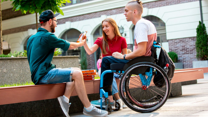 Kolme nuorta viettää aikaa ulkona. Yksi heistä istuu pyörätuolissa. 