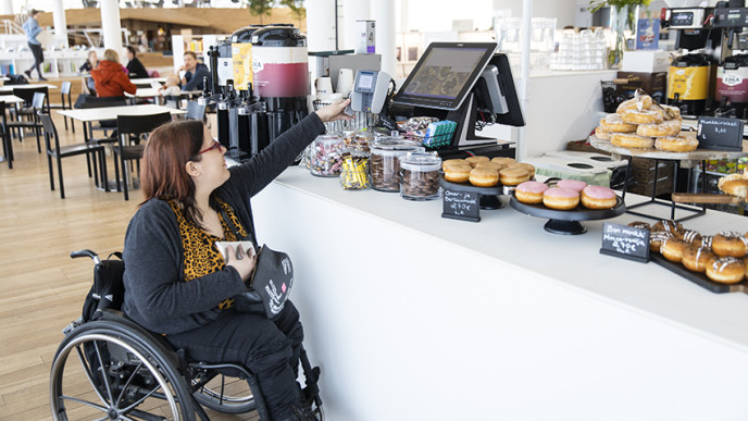 Pyörätuolia käyttävä nainen kurkottaa kohti maksupäätettä. 