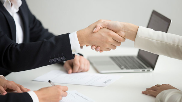 Ihmiset kättelevät pöydän yli. Kuvituskuva.