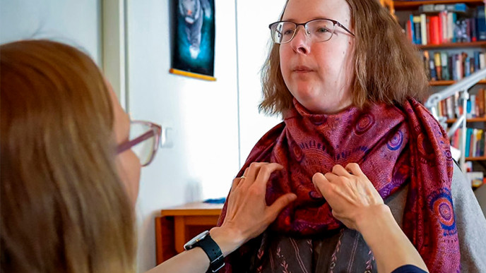 Henkilökohtainen avustaja auttaa henkilölle kaulahuivin kaulaan