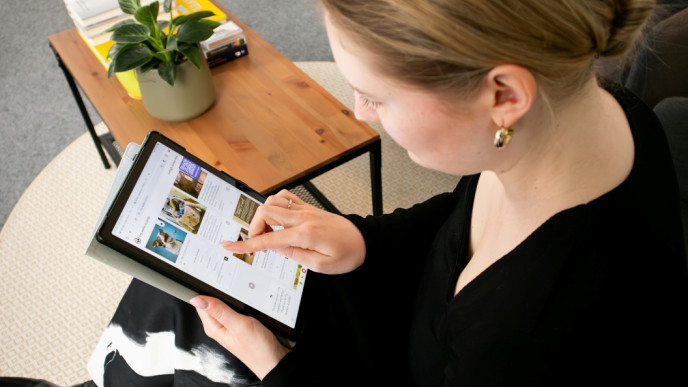 Istuva henkilö tutkii kämmentietokoneen näytöltä verkkosivua.