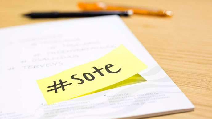 Pöydällä kynä, paperi ja muistilappu, jossa lukee sote